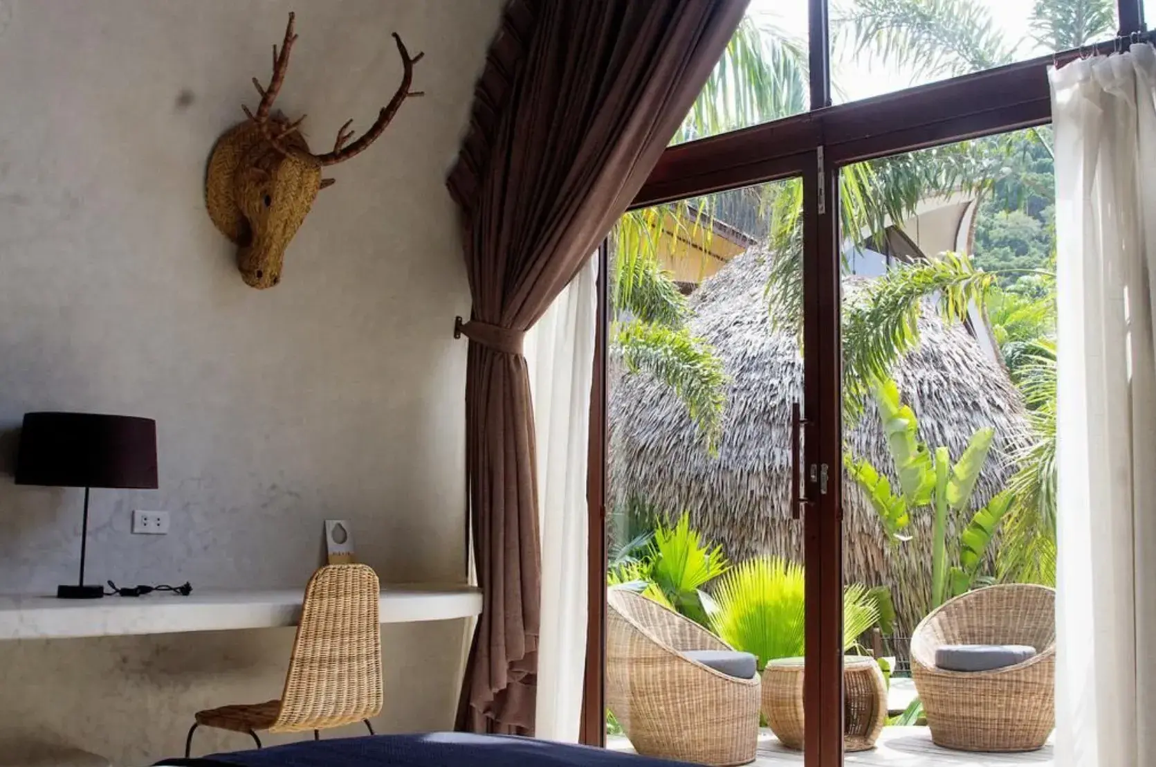 Suite Deluxe : baie vitrée avec rideaux, bureau et fauteuils en rotin sur le patio