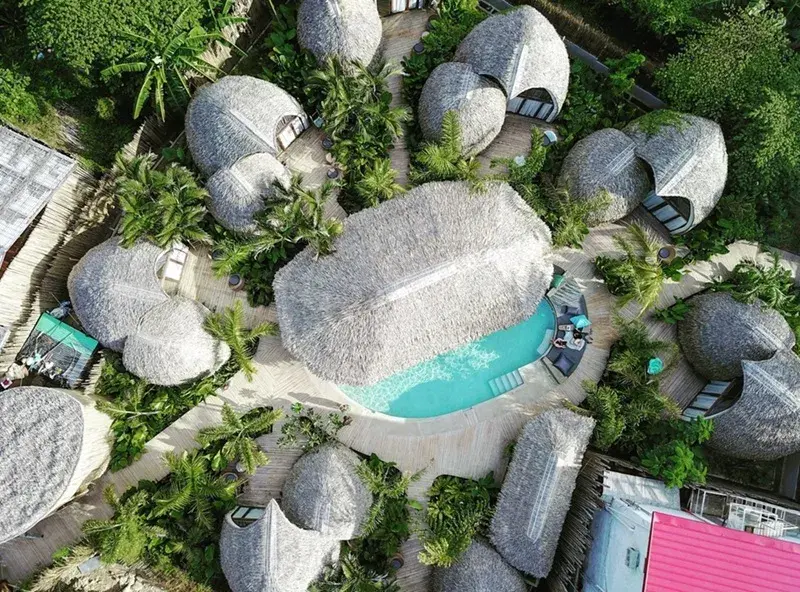 Cabanes au toit de chaume parmi les palmiers, autour de la piscine turquoise de l'hôtel