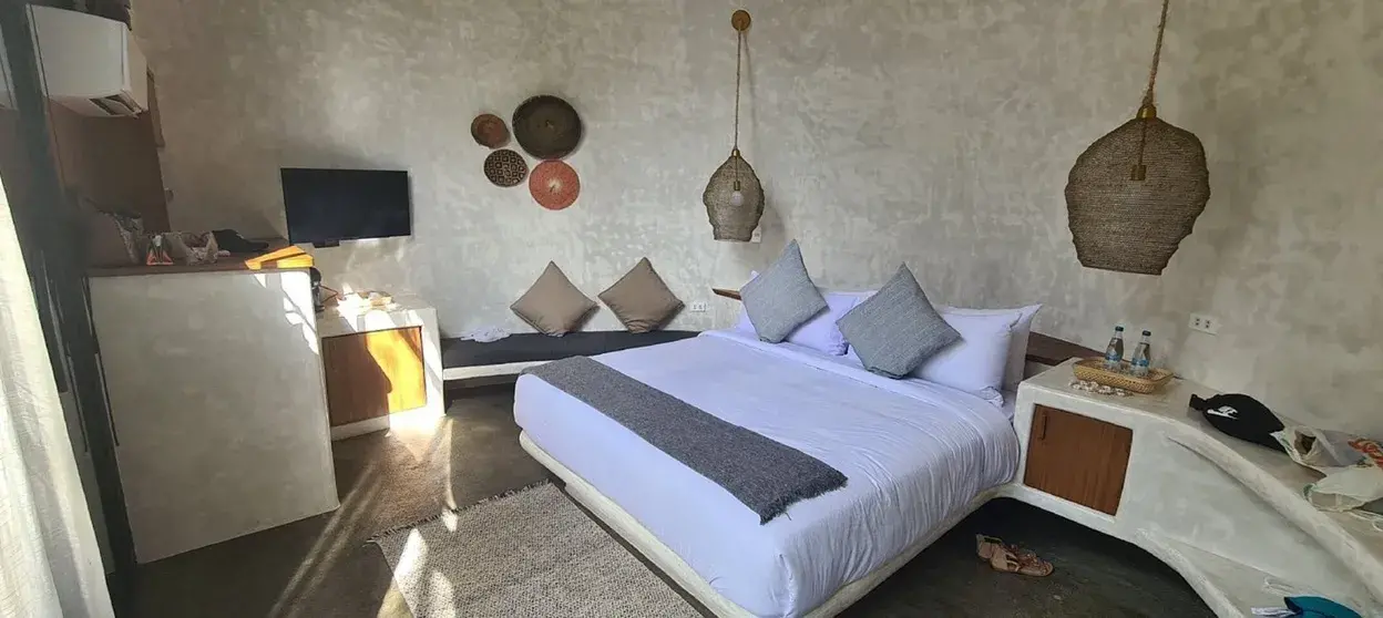 Chambre avec un grand lit en linge blanc, des suspensions en fibre, une télévision et un canapé-banc